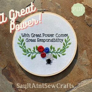 May include: Embroidered hoop art with the quote "With Great Power Comes Great Responsibility" surrounded by green leaves and red, blue, and white flowers. A black spider sits on a white web below the flowers. The words "A Great Power!" are written in pink above the hoop and "SayItAintSewCrafts" is written below the hoop.