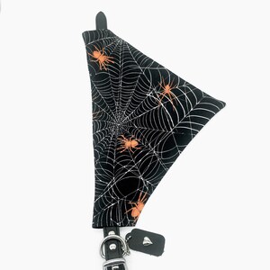 Op de afbeelding: Zwarte hondenbandana met een wit spinnenwebpatroon en oranje spinnen. De bandana is bevestigd aan een zwarte leren halsband met een zilveren gesp en een klein label.