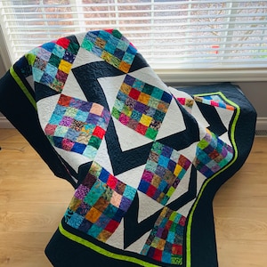 Peut inclure: Une courtepointe colorée en patchwork avec un motif géométrique noir et blanc. La courtepointe est pliée et drapée sur une chaise avec une bordure noire et verte.