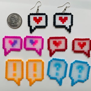 May include: A collection of pixelated speech bubble earrings and charms in various colors. The earrings feature a red heart design, while the charms display hearts, exclamation points, and question marks. The earrings have silver hooks.