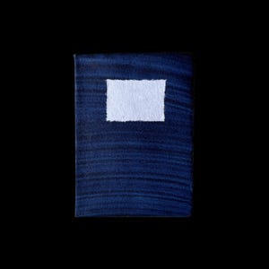 Puede incluir: Un pequeño cuaderno azul oscuro con una cubierta texturizada y una etiqueta rectangular blanca en la parte delantera. El cuaderno está sobre un fondo negro, resaltando su color y textura. El diseño es simple y minimalista.