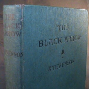 May include: A blue hardback book with the title "The Black Arrow" and the author's name "Stevenson" on the cover.