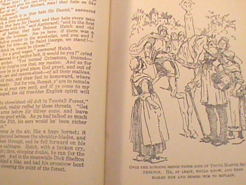 May include: A black and white illustration of a group of people on horseback. The people are dressed in medieval clothing and are riding through a forest. The text "Over the echoing bridge there rode up Young Master Dick Shelton. He, at least, would know, and then hailed him and begged him to explain." is at the bottom of the image.