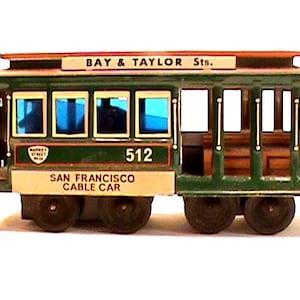 May include: A vintage San Francisco cable car toy, painted green and cream, with the text "BAY & TAYLOR Sts." and "SAN FRANCISCO CABLE CAR". The number "512" is visible on the side. The toy has four black wheels.