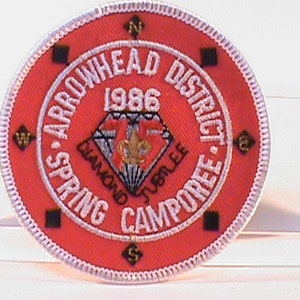Może przedstawiać: Naszywka haftowana w kolorze czerwonym, białym i niebieskim z tekstem "Arrowhead District Spring Camporee 1986 Diamond Jubilee" i wzorem róży wiatrów.