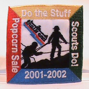 May include: A red, white, and blue embroidered patch with the text "Do the Stuff Scouts Do! Popcorn Sale 2001-2002".