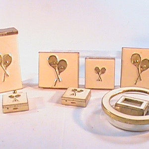 May include: Set of seven vintage vanity items with a light pink background and gold accents. The items feature a design of two tennis rackets crossed with a ball in the center.