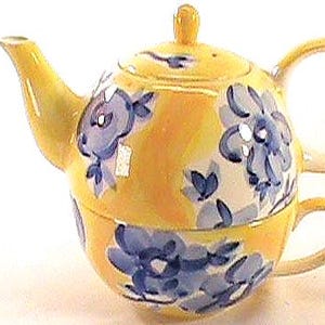 Puede incluir: Un juego de té individual de cerámica amarilla. Incluye una tetera con tapa y boquilla, y una taza que encaja debajo. Ambas piezas están decoradas con diseños florales azules.