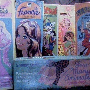 May include: A collection of vintage paper doll sets, including "Barbie," "Francie," "Chie," "Stevie Kyle," and "Magic Paper Doll." The boxes feature colorful illustrations of the dolls and characters. A box of "Sew Many Animals" is also visible.