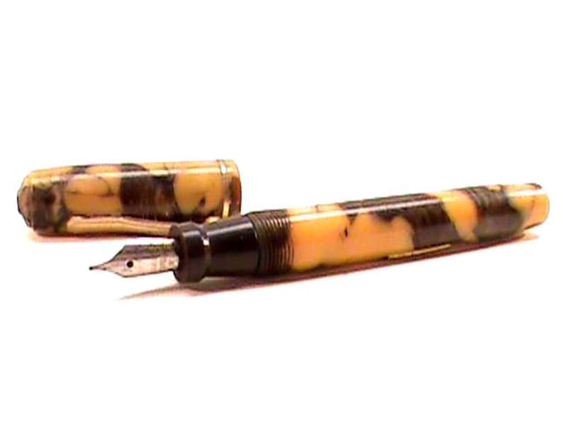 Puede incluir: Una pluma estilogr&aacute;fica vintage con un patr&oacute;n veteado en tonos amarillos y marrones. La pluma tiene una secci&oacute;n negra y un plum&iacute;n plateado. La tapa est&aacute; quitada, revelando el plum&iacute;n y el dise&ntilde;o de la pluma.