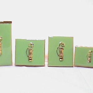 May include: Four different sized green and gold golf bag cufflinks. The cufflinks are rectangular and feature a gold golf bag with clubs sticking out of the top.