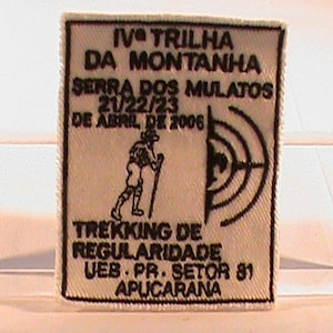 Puede incluir: Un parche blanco con texto negro y una ilustración en blanco y negro de un excursionista. El texto dice "IV^e TRILHA DA MONTANHA SERRA DOS MULATOS 21/22/23 DE ABRIL DE 2006 TREKKING DE REGULARIDADE UEB PR. SETOR 81 APUCARANA".