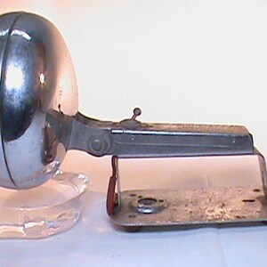 May include: A vintage chrome spotlight with a swiveling head and a base that can be mounted to a surface. The spotlight has a red accent on the base.