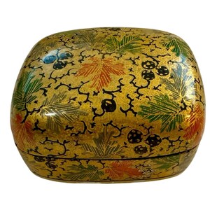 May include: A decorative, oval-shaped box with a lid. The box is painted gold with a leaf and berry design in green, orange, and black. The box has a glossy finish and appears to be made of wood or a similar material.