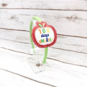 May include: A green headband with a red apple-shaped felt applique. The apple has a white center with the text "100 days smarter" in rainbow colors.