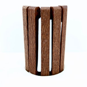 May include: A brown wooden cup holder with vertical slats. The holder has a curved shape and a white interior. The design is simple and modern, suitable for holding a beverage container.