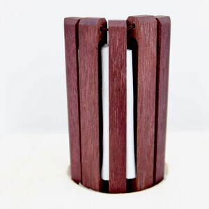 May include: A wooden paper towel holder with a white paper towel inside. The holder is made of dark brown wood and has a cylindrical shape.