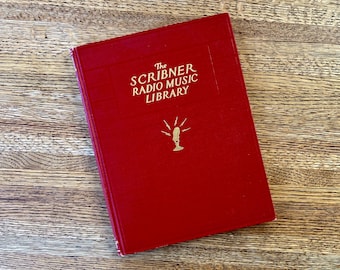 Könnte beinhalten: Ein rotes Hardcover-Buch mit goldenen Lettern, auf dem "The Scribner Radio Music Library" steht. Das Buch hat eine goldene Illustration eines Mikrofons mit strahlenden Linien.