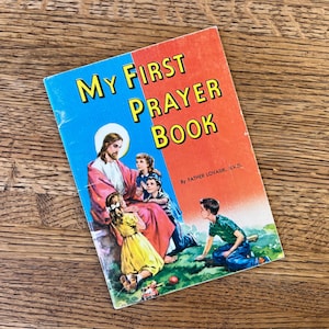 May include: A vintage children's prayer book titled "My First Prayer Book" with a blue and red cover. The cover features an illustration of Jesus with children. The book is by Father Lovasik, S.V.D.