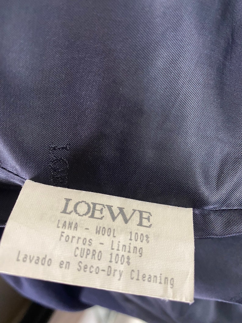 May include: A white tag with black text that reads "LOEWE", "LANA - WOOL 100%", "Forros - Lining", "CUPRO 100%", and "Lavado en Seco-Dry Cleaning".