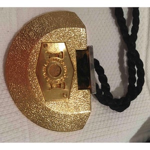 May include: A gold-colored, half-circle shaped pendant with a black cord. The pendant has a hexagonal design with the word "JOY" inscribed in the center.