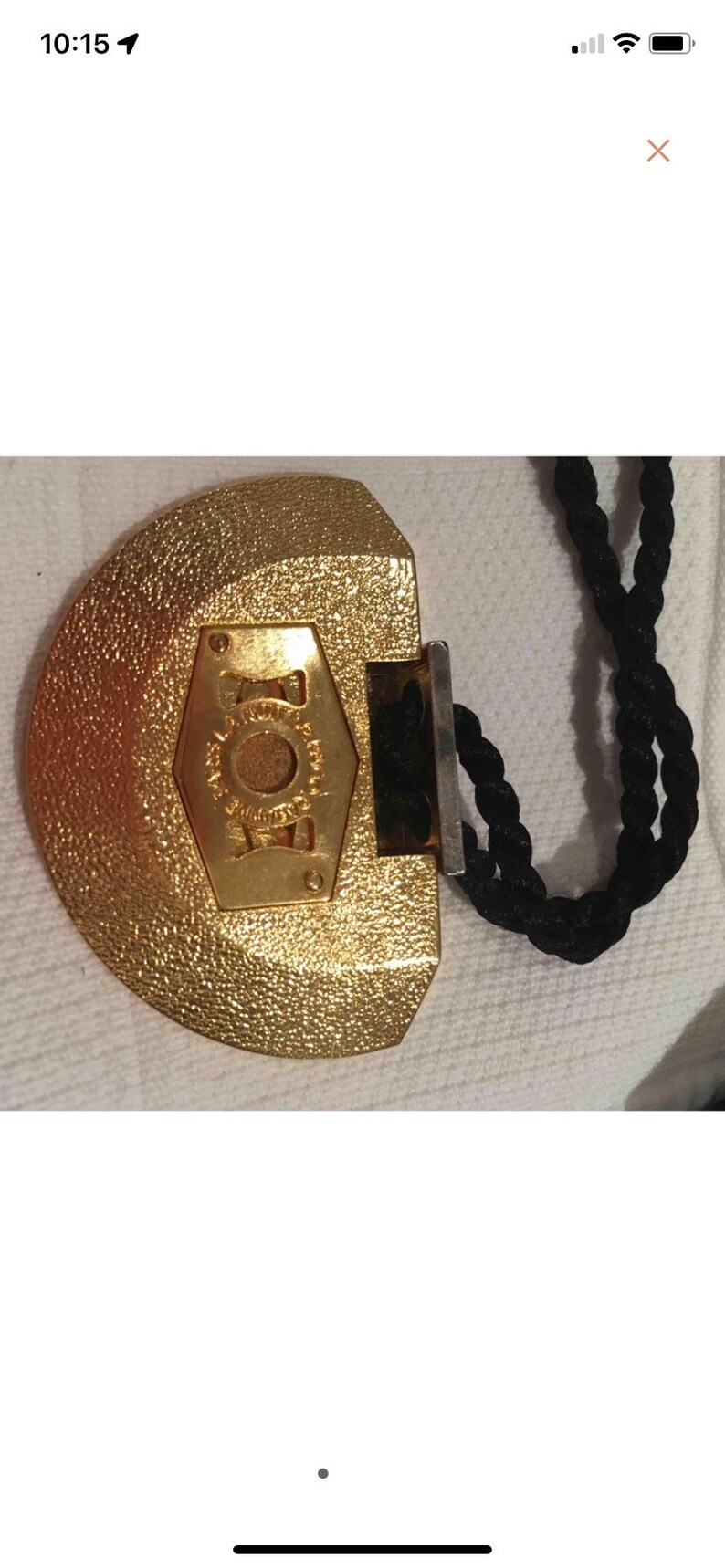 May include: A gold-colored, half-circle shaped pendant with a black cord. The pendant has a hexagonal design with the word "JOY" inscribed in the center.