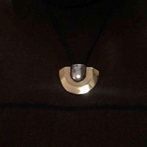 May include: A black necklace with a gold and silver pendant shaped like a crescent moon.
