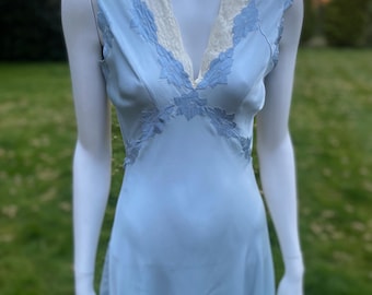 May include: A light blue sleeveless slip dress with a white lace trim around the neckline. The dress has a V-neck and a flowing skirt.
