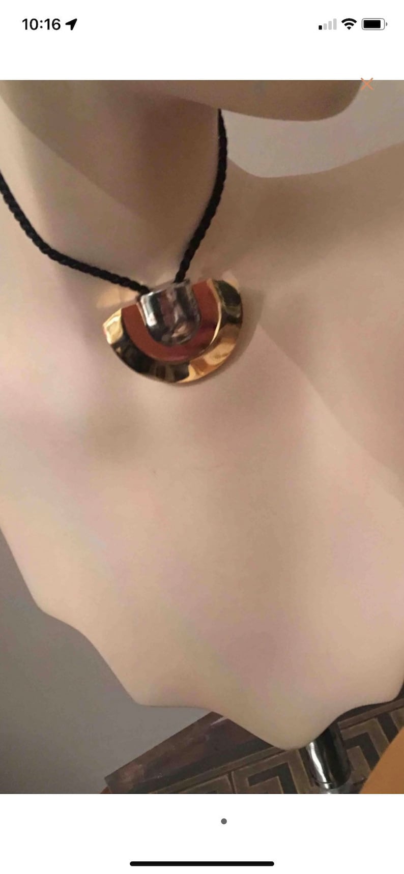 May include: A gold and silver pendant necklace with a black cord. The pendant is a geometric shape with a rounded top and a flat bottom.