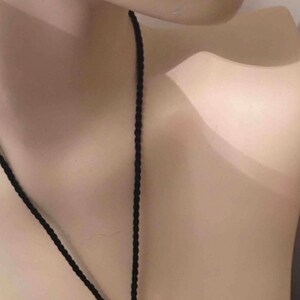 May include: A gold and silver pendant necklace with a black cord. The pendant is a half-circle shape with a textured surface.