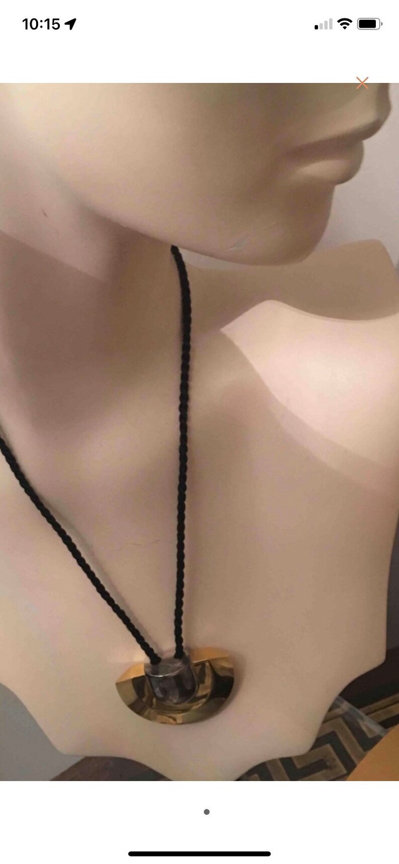 May include: A gold and silver pendant necklace with a black cord. The pendant is a half-circle shape with a textured surface.
