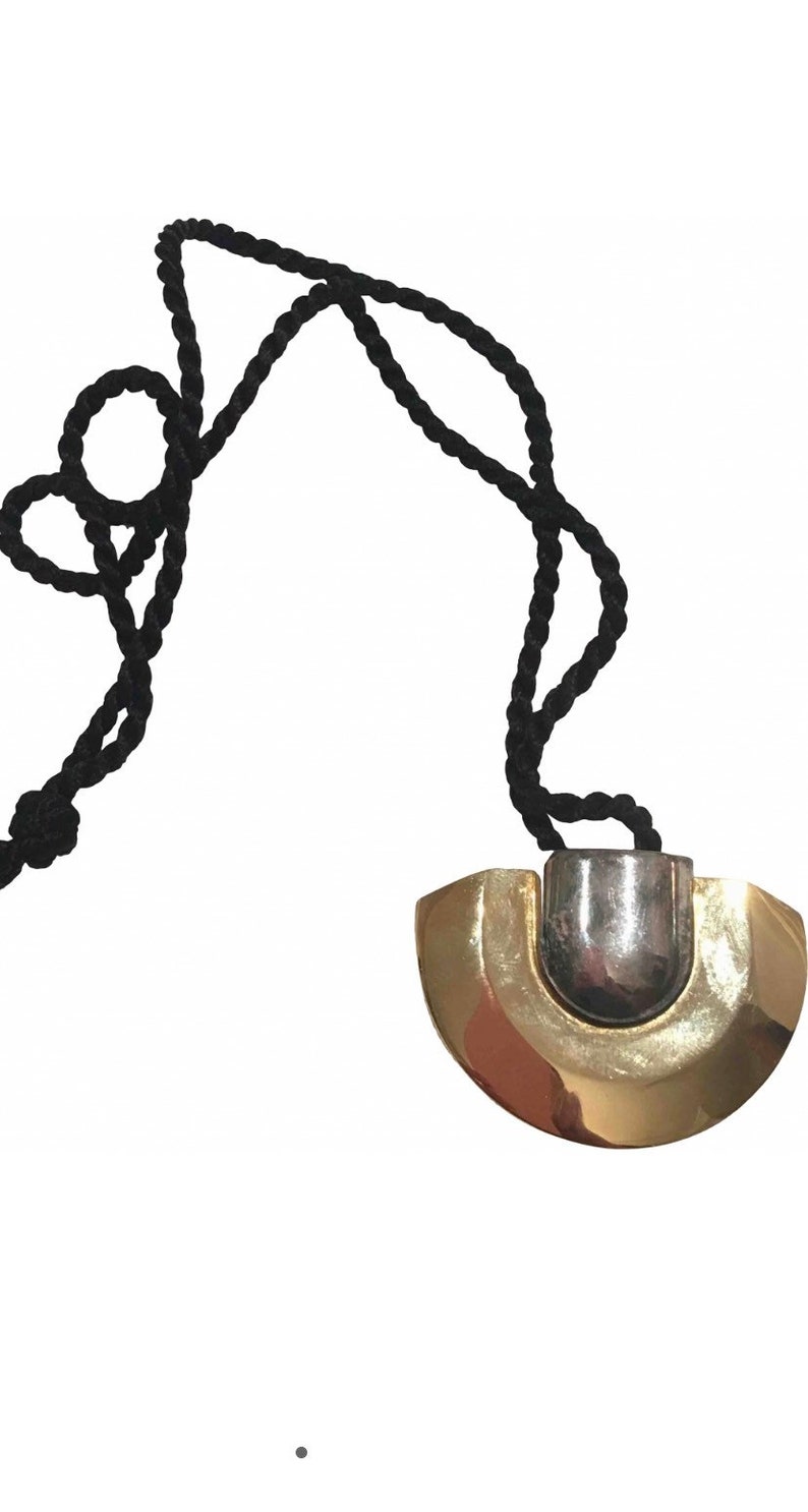 May include: A gold and silver pendant necklace with a black cord. The pendant is a half-circle shape with a silver center.