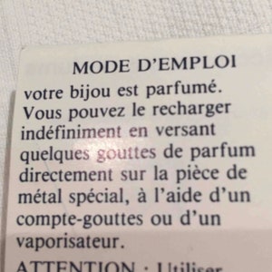 May include: A white card with black text explaining how to refill a scented jewelry piece. The text reads "MODE D'EMPLOI votre bijou est parfum&eacute;. Vous pouvez le recharger ind&eacute;finiment en versant quelques gouttes de parfum directement sur la pi&egrave;ce de m&eacute;tal sp&eacute;cial, &agrave; l'aide d'un compte-gouttes ou d'un vaporisateur. ATTENTION : Utiliser toujours le m&ecirc;me parfum."
