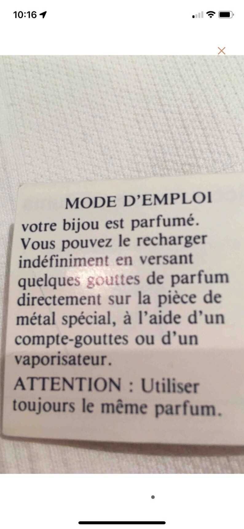 May include: A white card with black text explaining how to refill a scented jewelry piece. The text reads "MODE D'EMPLOI votre bijou est parfum&eacute;. Vous pouvez le recharger ind&eacute;finiment en versant quelques gouttes de parfum directement sur la pi&egrave;ce de m&eacute;tal sp&eacute;cial, &agrave; l'aide d'un compte-gouttes ou d'un vaporisateur. ATTENTION : Utiliser toujours le m&ecirc;me parfum."