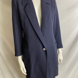 May include: A navy blue blazer and skirt suit with a single rhinestone button. The blazer has a long, fitted silhouette and a pointed collar.