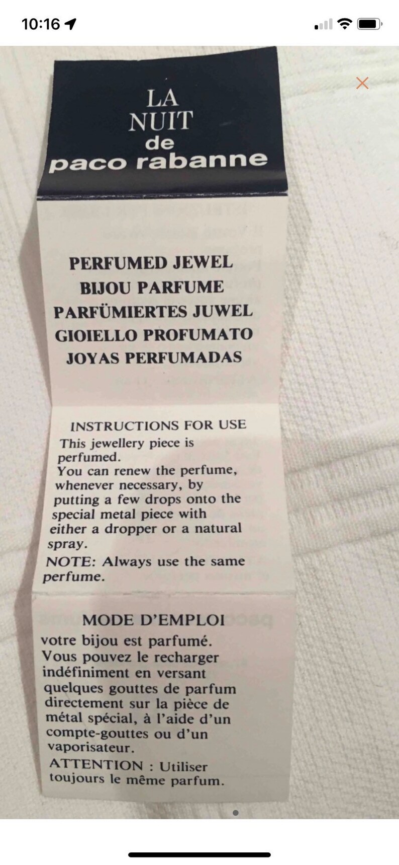 May include: A white label with black text that reads "LA NUIT de paco rabanne" and instructions for use for a perfumed jewel. The text reads "PERFUMED JEWEL, BIJOU PARFUME, PARF&Uuml;MIERTES JUWEL, GIOIELLO PROFUMATO, JOYAS PERFUMADAS". The instructions for use are in English and French.