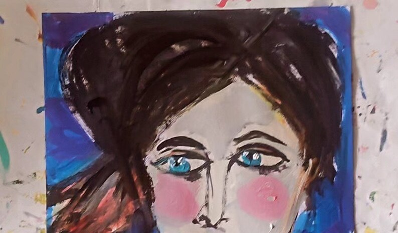 以下が含まれることがあります： 青い目をした女性の顔の絵。頬はピンクで、髪は黒。背景は濃い青色です。
