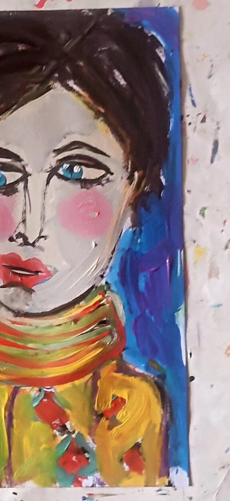 以下が含まれることがあります： 青い目と赤い唇をした人のカラフルな絵画。その人は黄色、緑、赤のストライプのシャツを着ています。背景は青です。