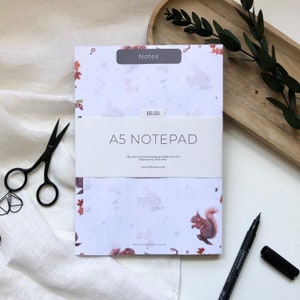 Könnte beinhalten: Ein weißer A5-Notizblock mit einem Aquarell-Design aus Eichhörnchen und Blättern. Der Notizblock hat 50 Blatt Recyclingpapier und wird in Großbritannien hergestellt. Der Preis beträgt 6,50 £.