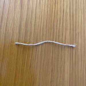 May include: A close-up of a single strand of natural twine or string on a wooden surface.