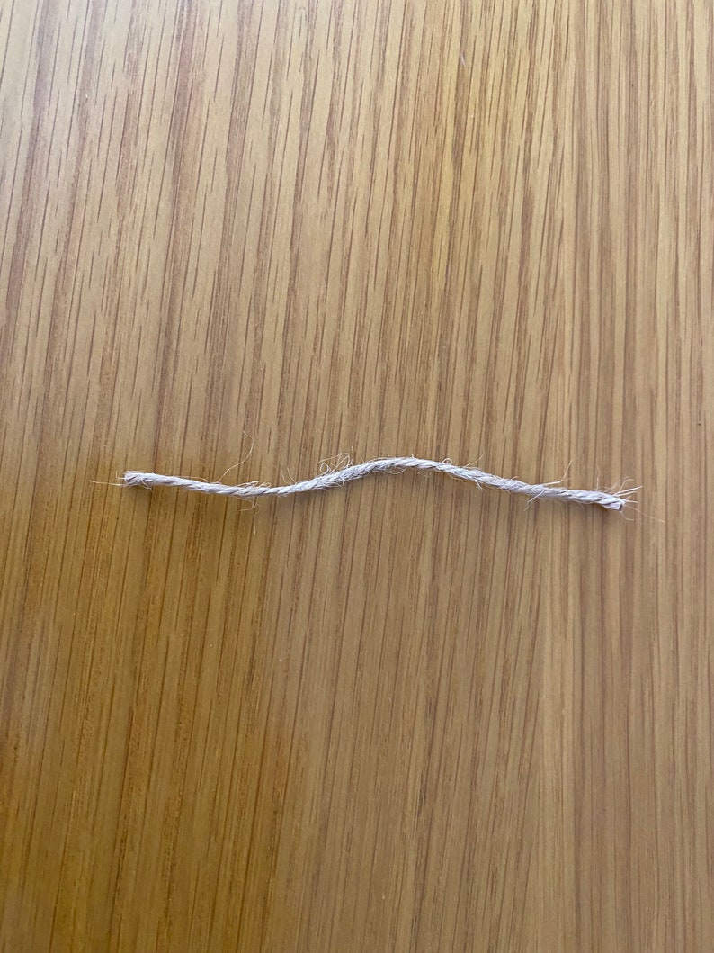 May include: A close-up of a single strand of natural twine or string on a wooden surface.