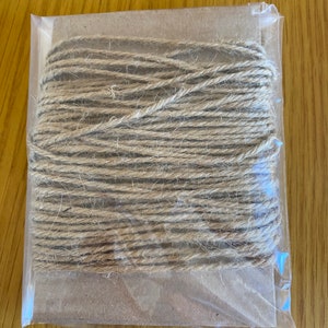 May include: A roll of natural twine wrapped in a clear plastic bag. The twine is brown and has a rough texture.