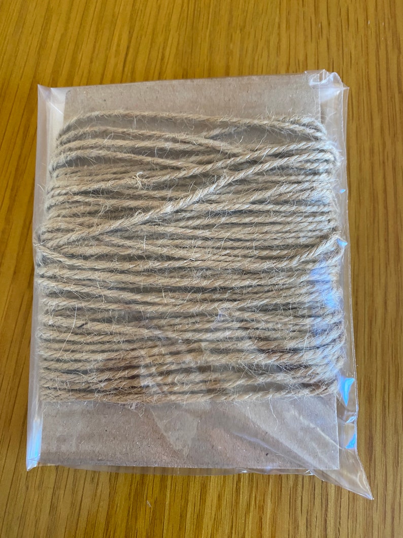 May include: A roll of natural twine wrapped in a clear plastic bag. The twine is brown and has a rough texture.