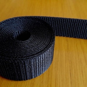 May include: A roll of black nylon webbing, a type of strong, durable fabric often used for straps, belts, and other applications.
