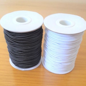 May include: Two spools of elastic cord, one black and one white. The spools are made of white cardboard and have a hole in the centre.