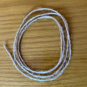 May include: A close-up of a coil of natural twine, a type of string made from natural fibres, on a wooden surface.