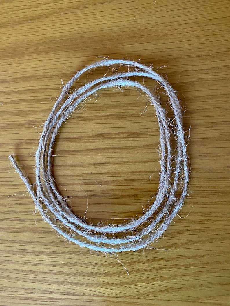 May include: A close-up of a coil of natural twine, a type of string made from natural fibres, on a wooden surface.