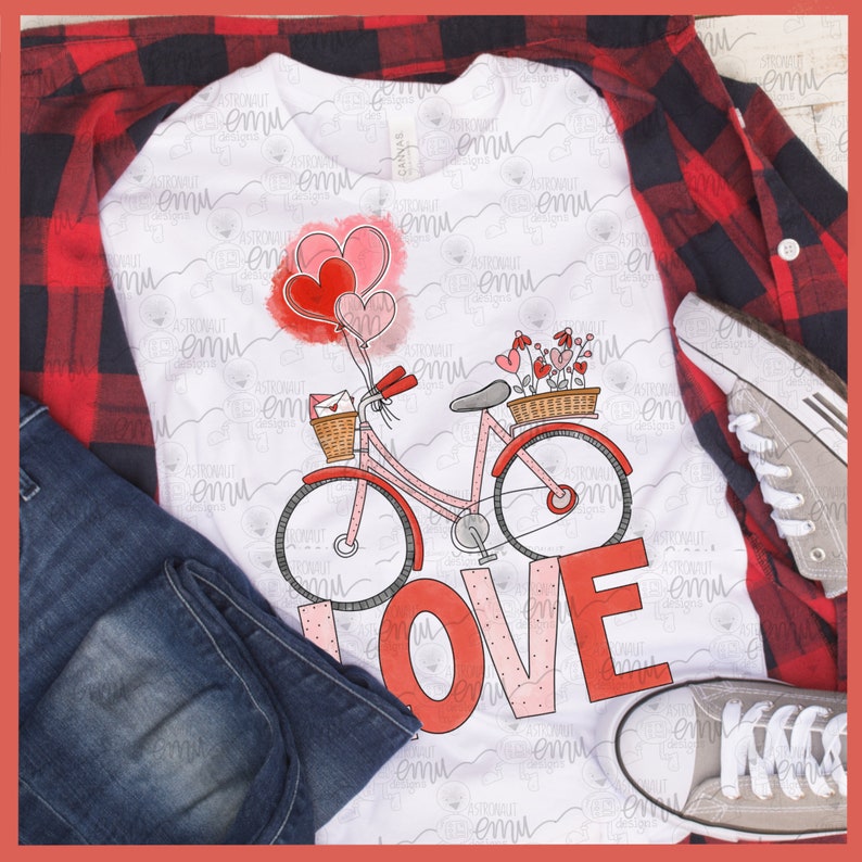 Pu&ograve; includere: Una maglietta bianca con una bicicletta rosa che trasporta un cestino di fiori e un cestino con una lettera. La bicicletta ha palloncini rossi attaccati al manubrio. La parola "LOVE" &egrave; scritta in grandi lettere rosse con pois bianchi.