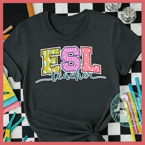 May include: Dark gray t-shirt with the text "ESL teacher" in colorful, block letters. The letters are yellow, pink, and red with decorative patterns. The shirt is knotted at the bottom.
