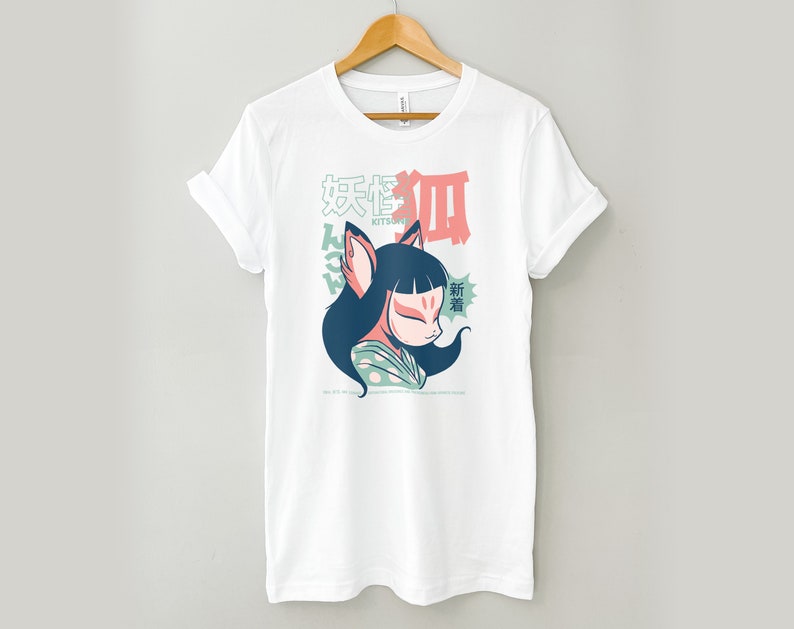 Peut inclure: T-shirt blanc avec un imprim&eacute; graphique d'un kitsune (esprit renard japonais) portant un masque et un kimono &agrave; motifs vert et blanc. Le texte "Kitsune" et des caract&egrave;res japonais sont imprim&eacute;s sur le t-shirt.